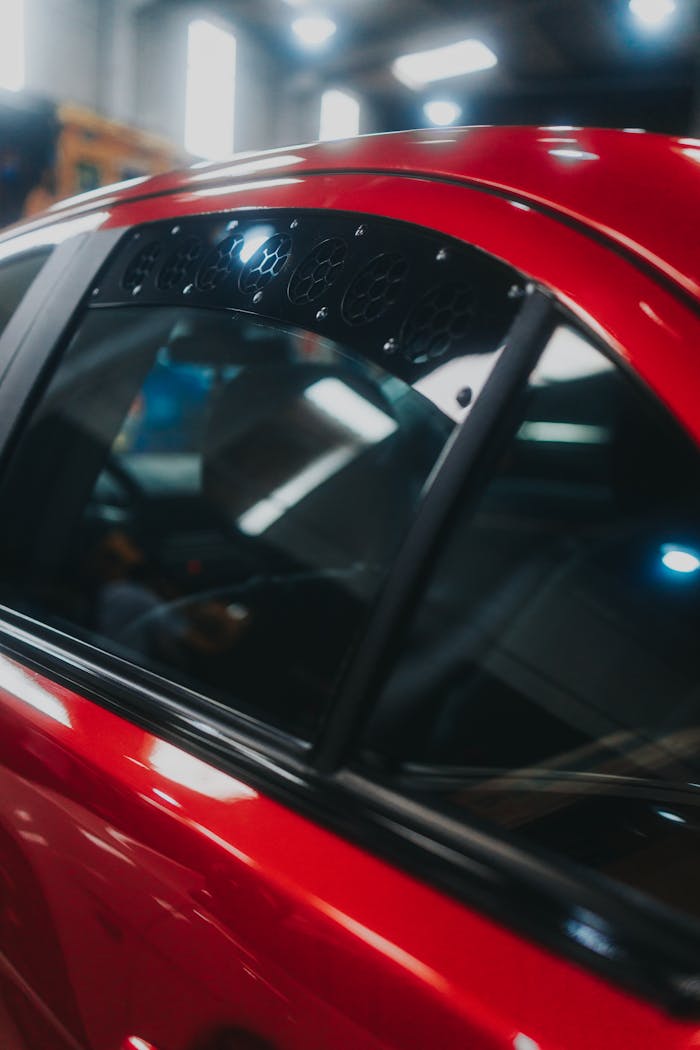 A focused shot of a red car's side window reflecting indoor lights.
