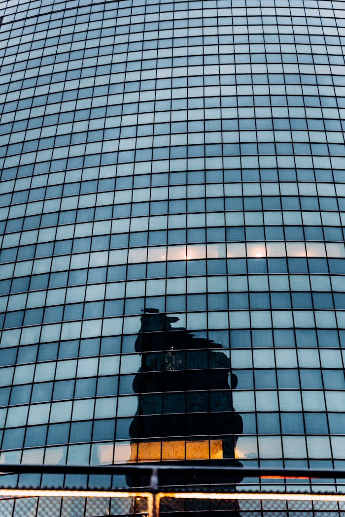 Tall glass building reflecting shadow of an iconic structure, showcasing urban architecture.